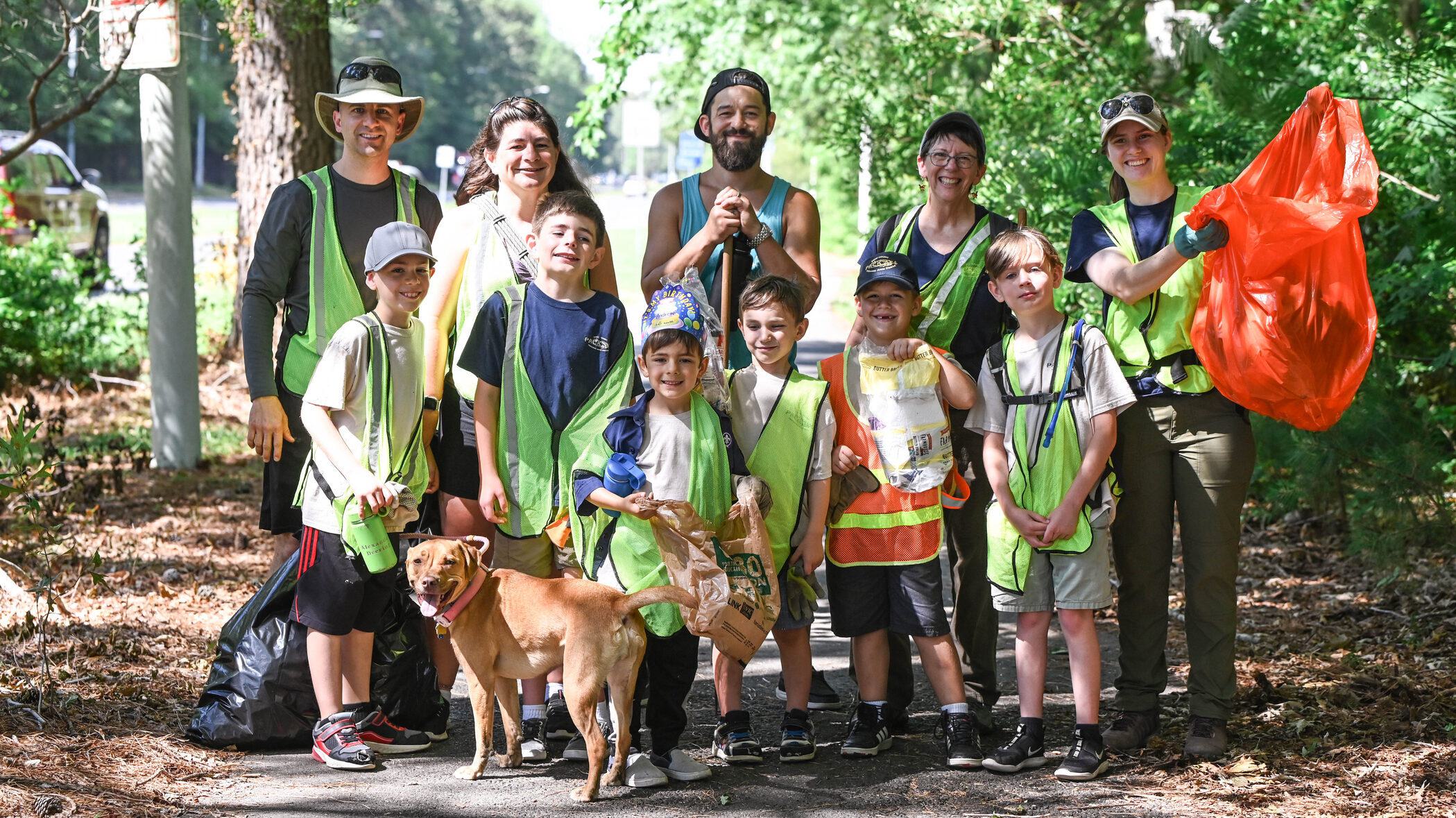 A group of adult and youth volunteers in high-vis vests (plus a dog) pose for a photo on Clean the Bay Day.