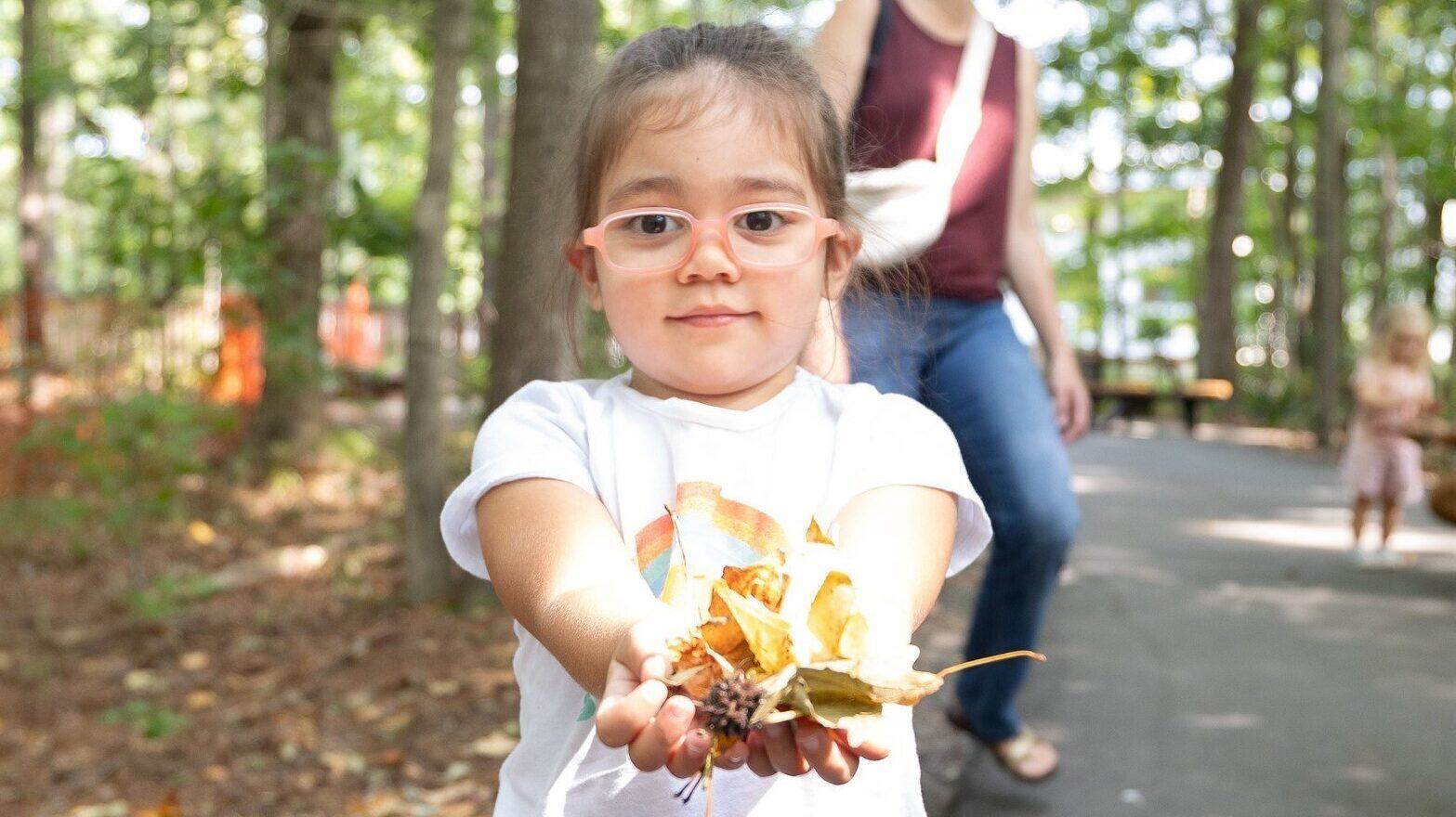 Toddler girl holds up leaves collected during Toddler Trek on Nature Trail