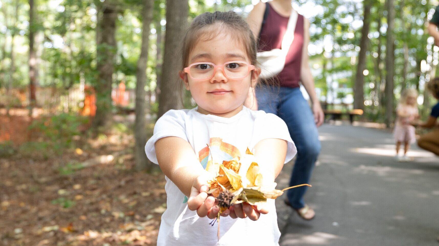 Toddler girl holds up leaves collected during Toddler Trek on Nature Trail