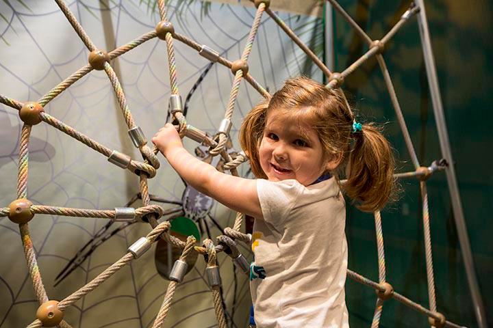 Young girl climbs rope shaped like a spider web