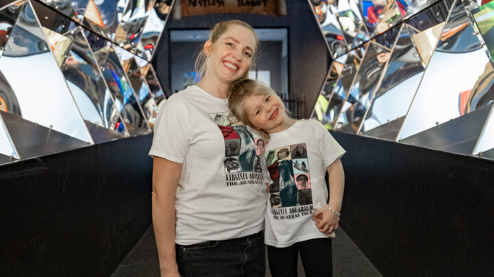 A parent and their child pose in the Reflections Gallery wearing AquaEras Tour shirts.